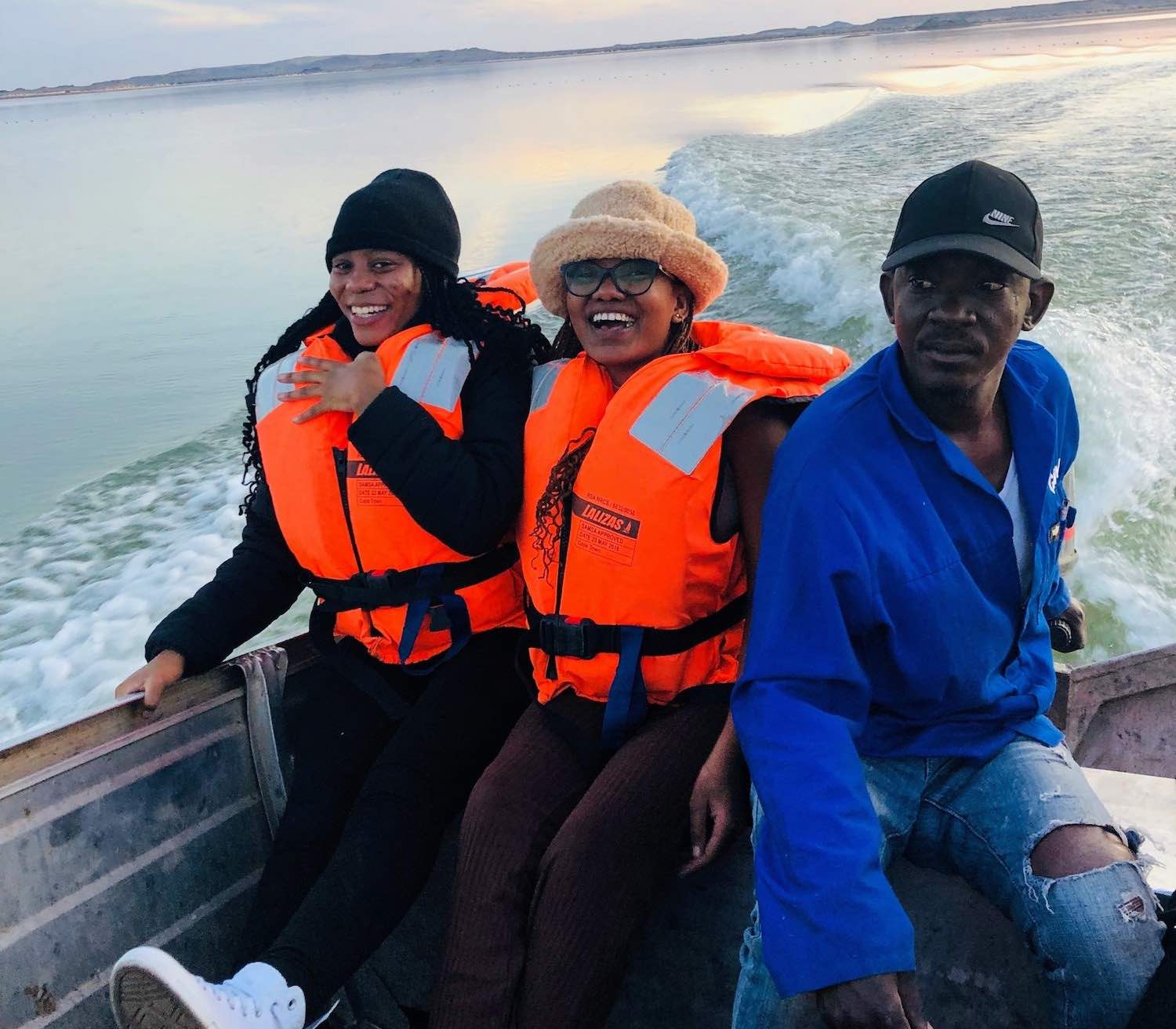 Two smiling women sit next to the steersman in a small boat.