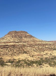 A mountain with short grass and shrubs at the bottom