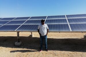 A man stands in front of a bank of solar panels.